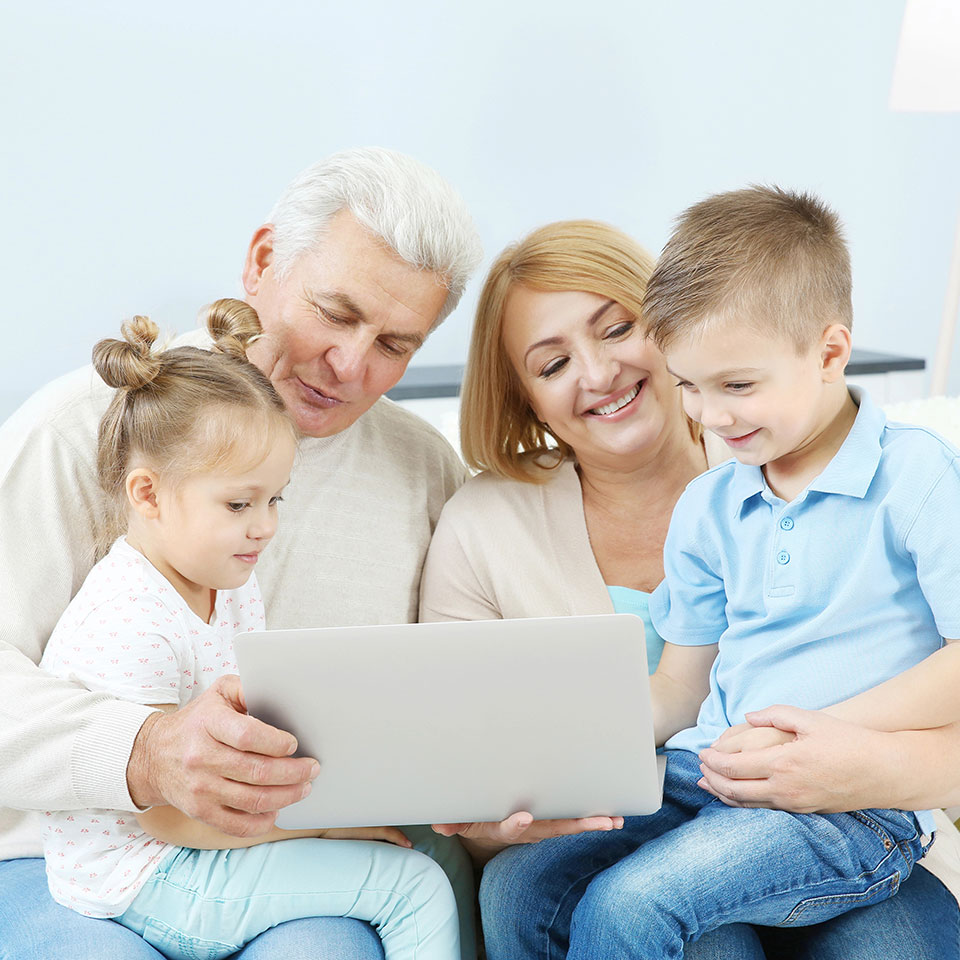 An older couple with their two grandkids on their laps, laughing at family photos on a laptop computer.